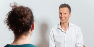 Christoph im Gespräch mit einem Klienten mit humorvollem Gesichtsausdruck.