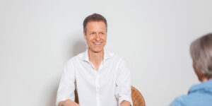 Christoph lächelt sympathisch im Gespräch mit einer Klientin.