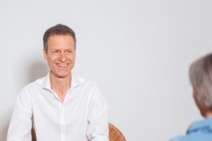 Christoph lächelt eine Klientin an, die ihm gegenübersitzt.